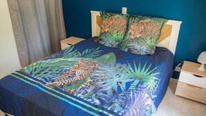 Ein Bett mit Leopardenmuster-Bettdecke und passenden Kissen, ein Nachttisch aus Holz und ein weißer Beistelltisch mit Lampe.