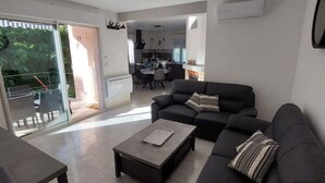Ein modernes Wohnzimmer mit einem dunklen Sofa, einem Couchtisch und einem Essbereich im Hintergrund.