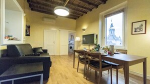 A living room with a sofa, a dining table with chairs, a TV, and a window with a view of a building. - Penthouse with fantastic views of the monuments of Rome!
Free wi-fi (Roma)