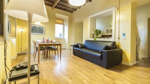 A living room with a dark-colored sofa, a dining table with chairs, a lamp, and a ceiling with exposed beams. - Penthouse with fantastic views of the monuments of Rome!
Free wi-fi (Roma)