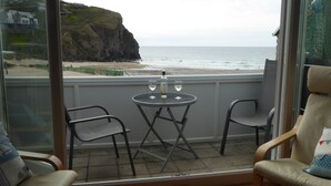 A balcony with two chairs and a small table, overlooking a beach and cliffs. - Beach side Accommodation, Porthtowan, SATURDAY CHANGEOVER ONLY (Porthtowan)