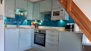 A compact kitchen with light blue cabinets, a microwave, a stove, and a sink. - Beach side Accommodation, Porthtowan, SATURDAY CHANGEOVER ONLY (Porthtowan)