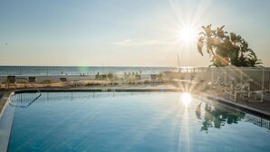 Una piscina azul cristalina con rayos de sol, una valla y vistas a la playa.