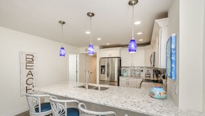 Cocina con encimera de mármol, electrodomésticos de acero inoxidable e iluminación colgante.