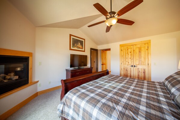 Um quarto com uma cama, um ventilador de teto, uma porta de madeira e uma televisão sobre um aparador.