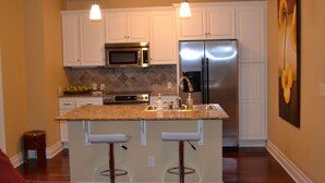 A kitchen with white cabinets, stainless steel appliances, a granite countertop, and two bar stools. - 6th Floor Condo in The Dickson with View of Old Main (Fayetteville)