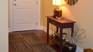 A hallway with a wooden floor, a white door, a lamp on a wooden console table, and a mirror on the wall. - 6th Floor Condo in The Dickson with View of Old Main (Fayetteville)