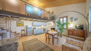 Amplia sala de estar con una mesa de comedor, sofás, una escalera, una cocina y un televisor.