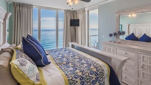 A bedroom with a large bed, a ceiling fan, a TV, a dresser, and a view of the ocean. - Beautifully Condo BOOK TODAY (Navarre)