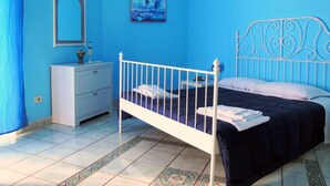 Ein Schlafzimmer mit einem weißen Metallbettgestell, einer blauen Wand, einer weißen Kommode und einem Fliesenboden.