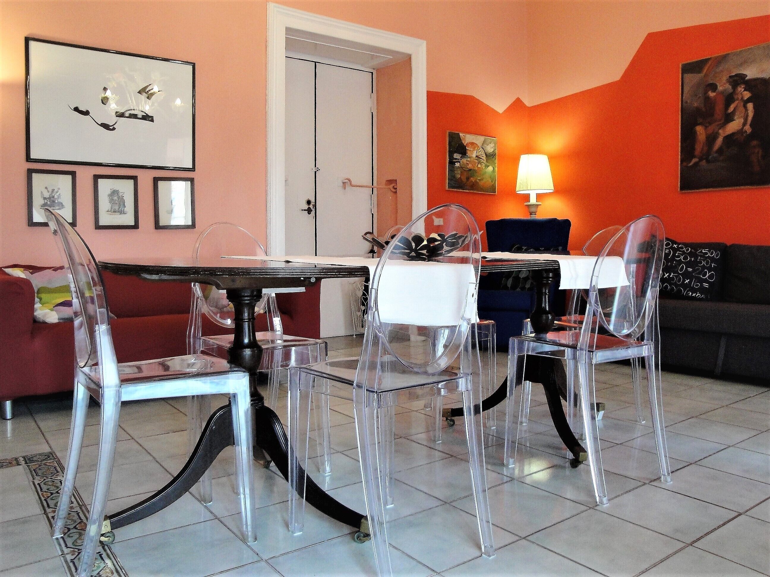 Uma sala de estar moderna com uma mesa de jantar, cadeiras transparentes, um sofá e obras de arte nas paredes.