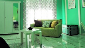 Ein Zimmer mit grüner Wand, einem grünen Sofa mit gemusterten Kissen, einem weißen Tisch und einem Koffer.