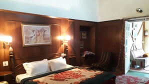 Une chambre d’hôtel avec un lit, deux lampes de chevet, une chaise, une tête de lit en bois, un tableau au mur et une vue sur l’extérieur.