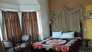 Une chambre d’hôtel avec un grand lit, deux chaises, une petite table et une fenêtre avec des rideaux.