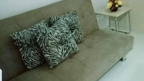 Un salon moderne avec un canapé gris, des coussins à motifs zébrés et une petite table d’appoint sur laquelle est posé un vase de fleurs.