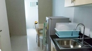 Une petite cuisine équipée d’un évier, d’une cuisinière et de placards. Un tissu à carreaux est accroché à la porte et un tapis bleu recouvre le sol.