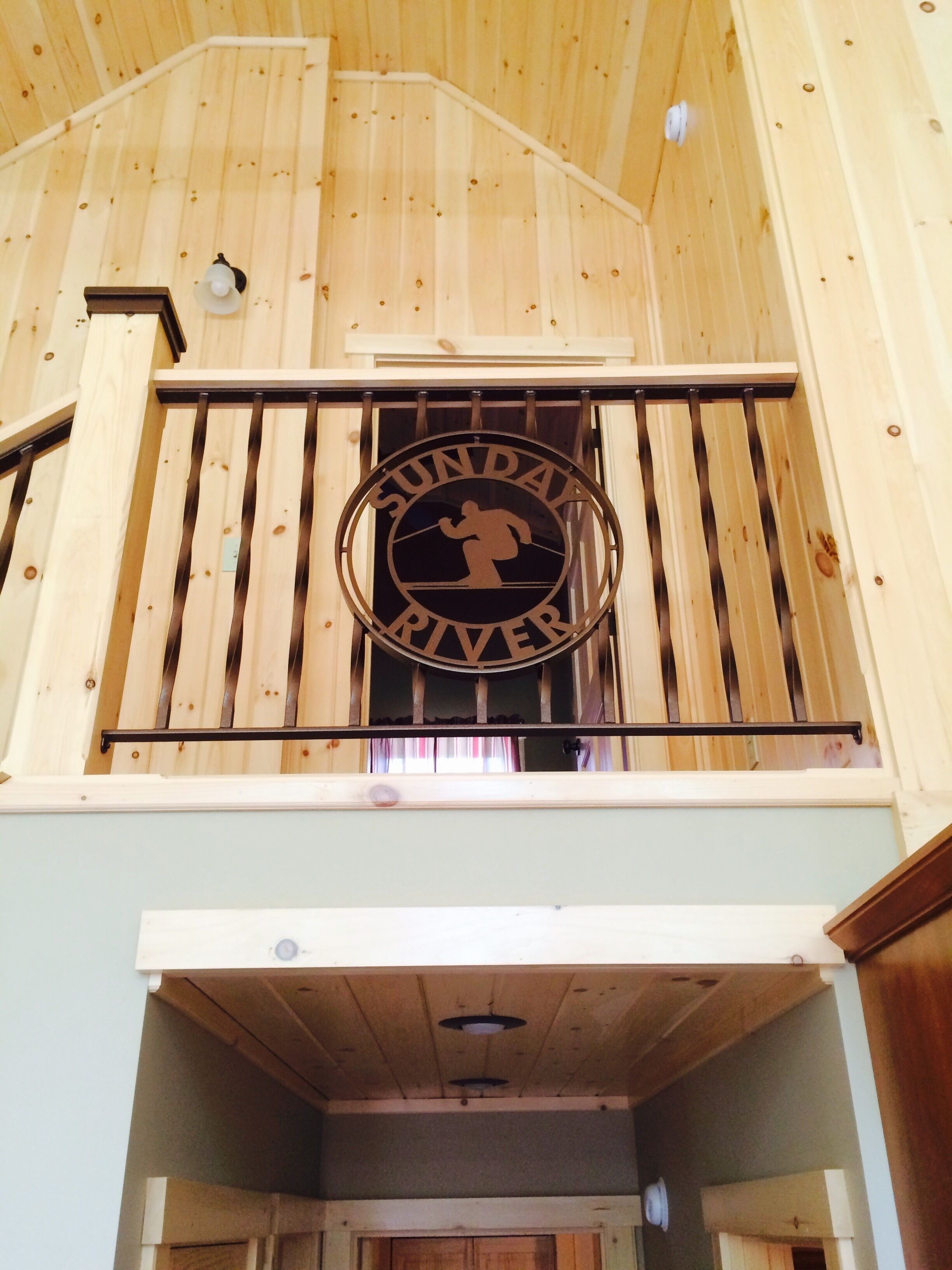 A wooden interior with a sign reading "SUNDAY RIVER" on a balcony railing.