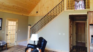 Un vaste espace de vie agrémenté d’un escalier en bois, d’un fauteuil en cuir noir et d’une lampe.