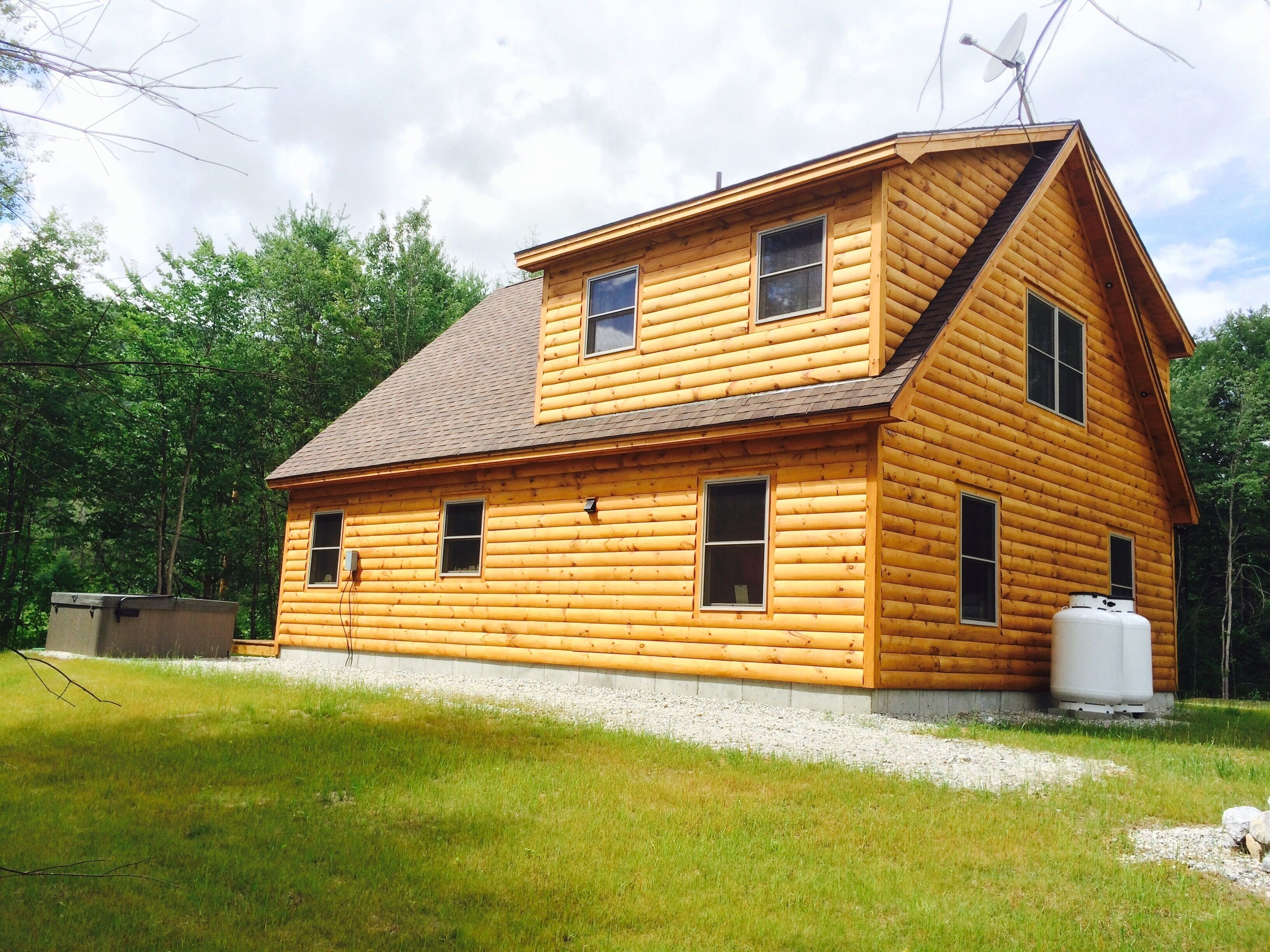 A two-story log cabin with a sloped roof, multiple windows, and a satellite dish.