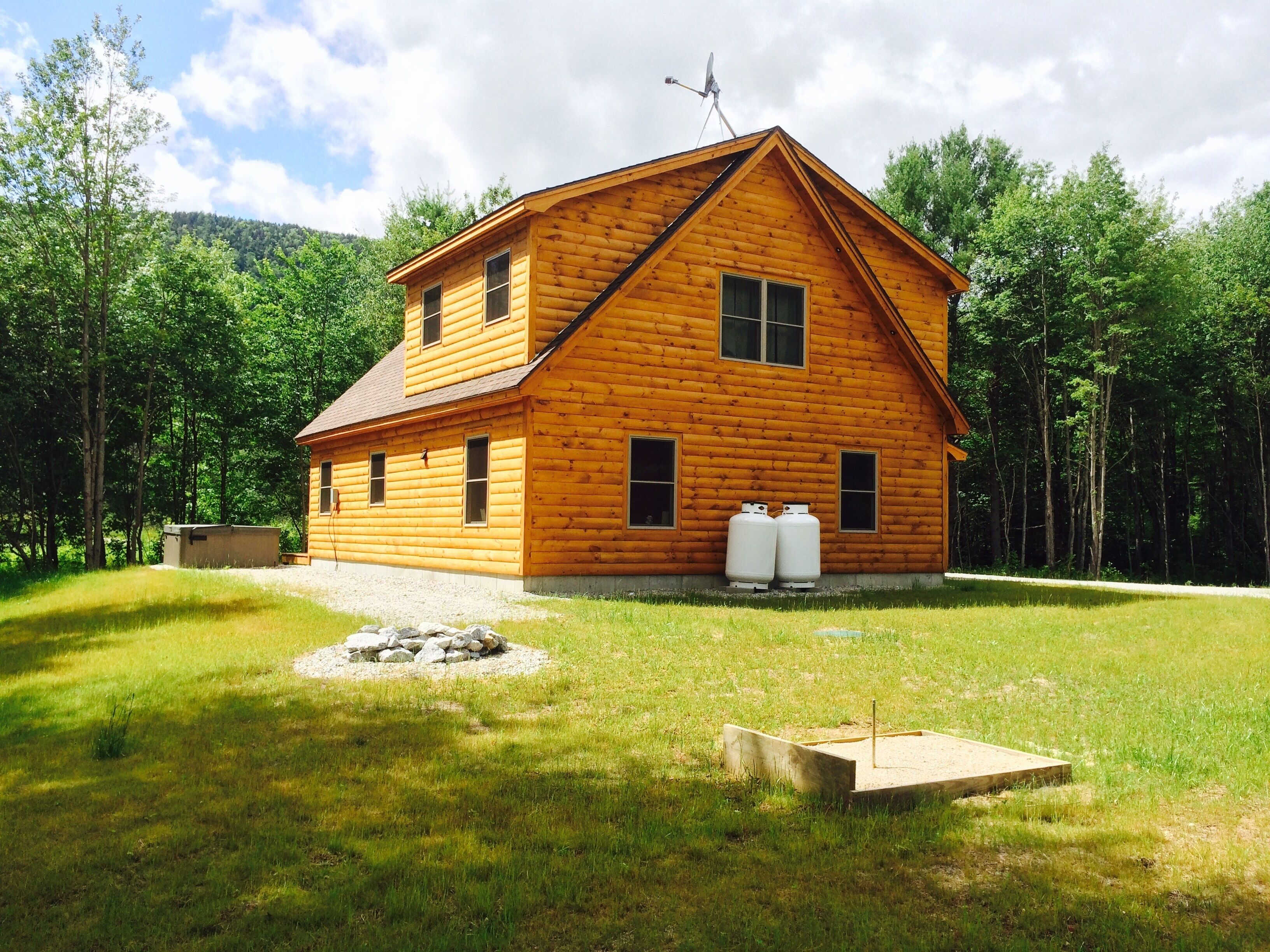 A log cabin with a chimney, a satellite dish, and propane tanks.