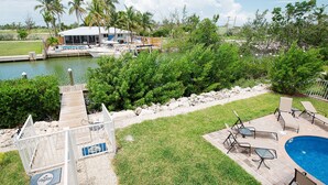 A pool area with lounge chairs, a small pool, and a dock with boats. - Stunning & Welcoming Pool Home on Canal (Marathon)