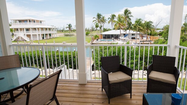A covered outdoor area with a table and two wicker chairs, overlooking a pool and buildings. - Stunning & Welcoming Pool Home on Canal (Marathon)