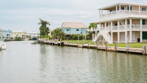 A waterfront property with a dock extending into calm water, surrounded by palm trees and a row of colorful buildings. - Stunning & Welcoming Pool Home on Canal (Marathon)