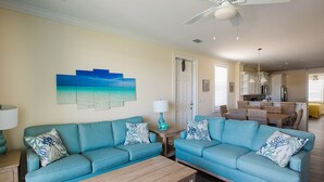 A living room with two teal sofas, a wooden coffee table, and a wall-mounted painting of a beach scene. - Stunning & Welcoming Pool Home on Canal (Marathon)