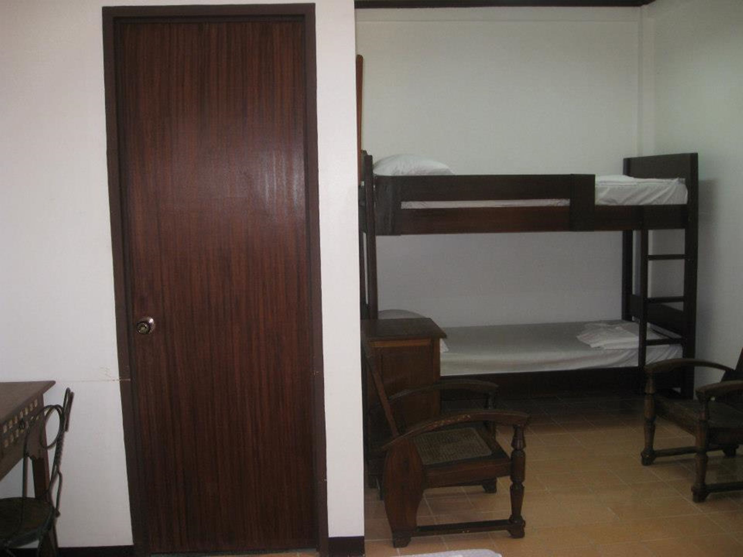 A room with a bunk bed, a wooden door, and a chair.