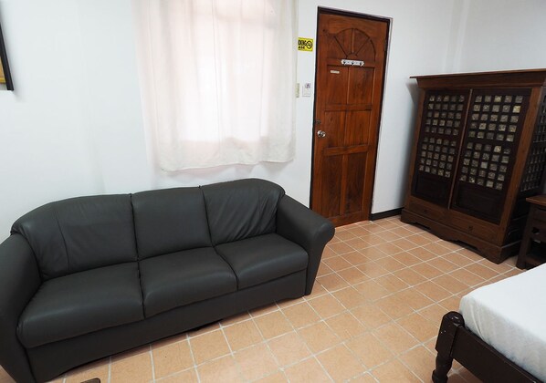 A room with a black leather sofa, a wooden wardrobe, and a bed with a white bedspread.