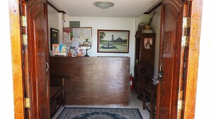 An entrance with a wooden archway leading to a reception desk, a blue patterned rug, and a tiled floor. - Balay Travel Lodge (Paoay)