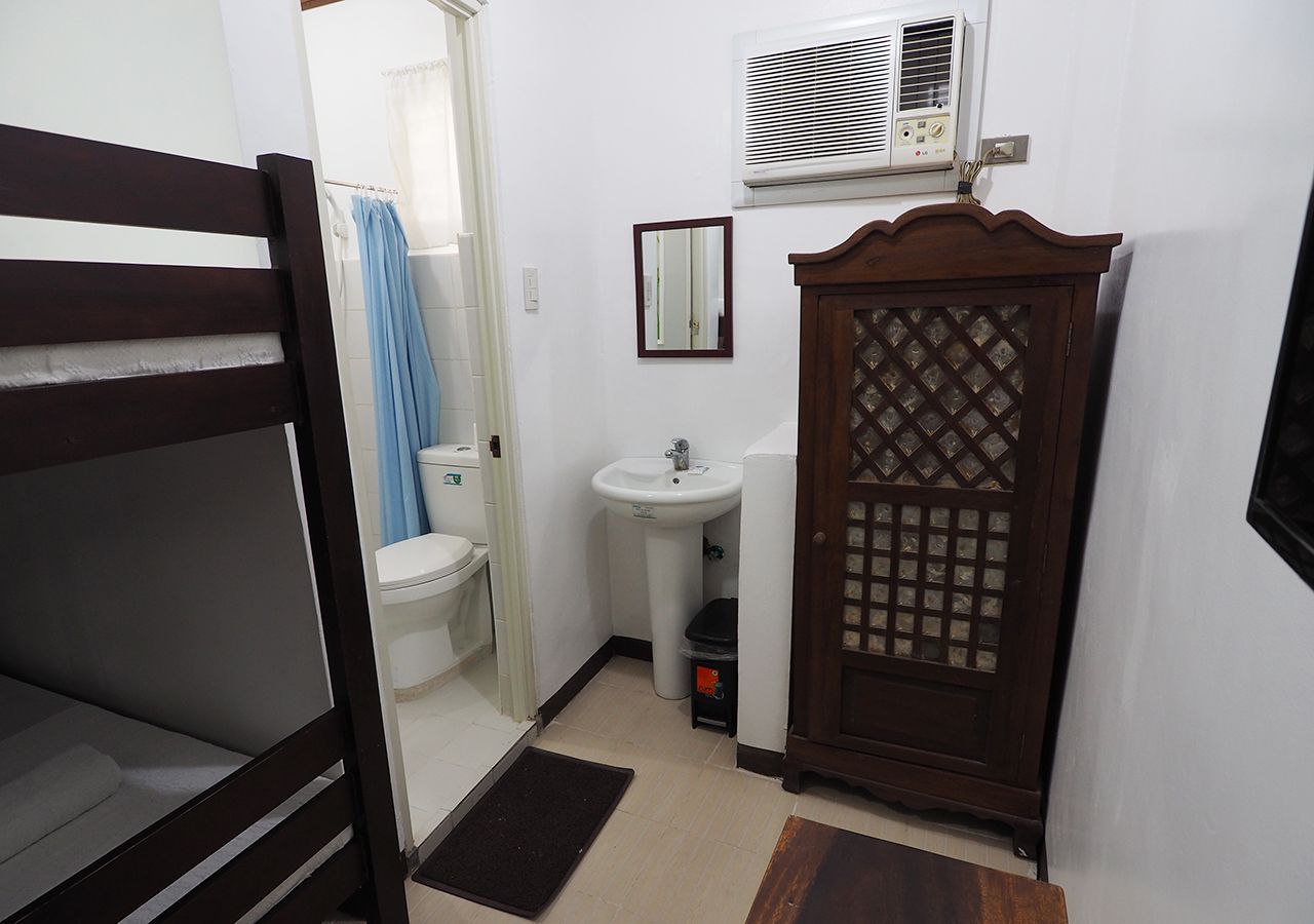 Quarto compacto com beliche, pia pequena, vaso sanitário e guarda-roupa com design vazado.