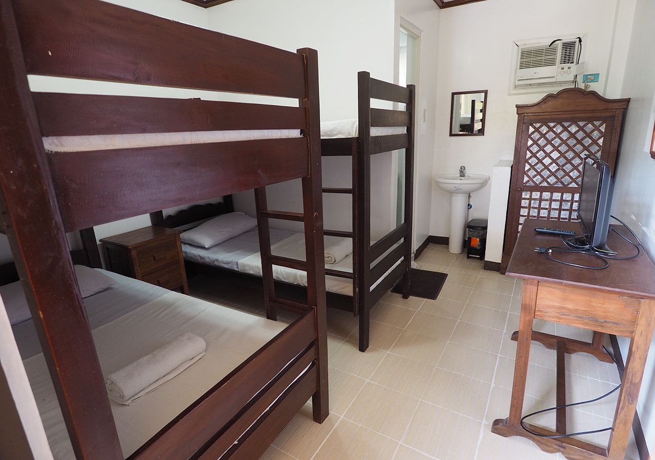 A room with two bunk beds, a wooden desk, a sink, and a mirror.
