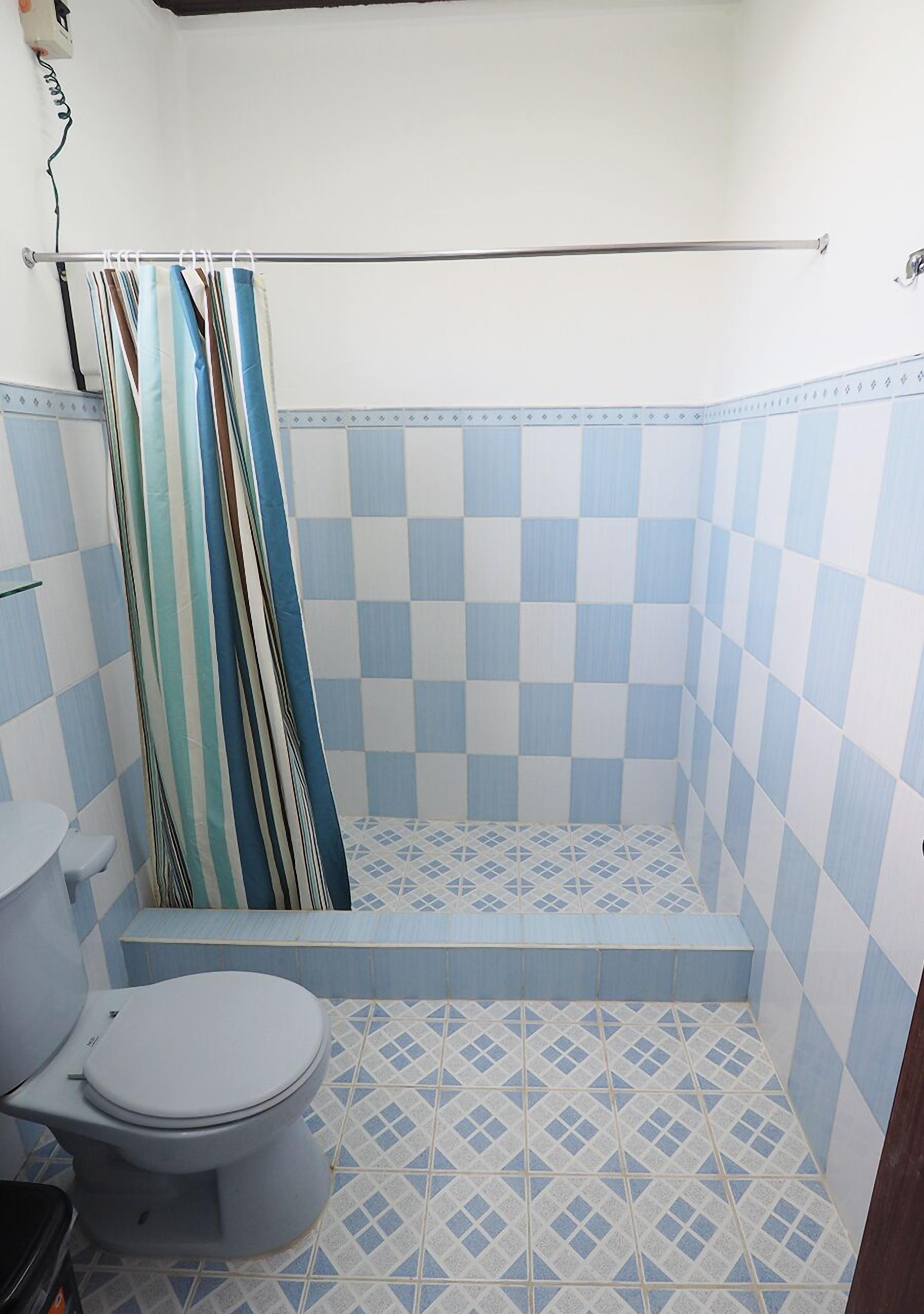 Een badkamer met toilet, een douchegedeelte met een zwart-wit betegelde vloer, en een handdoekhouder.