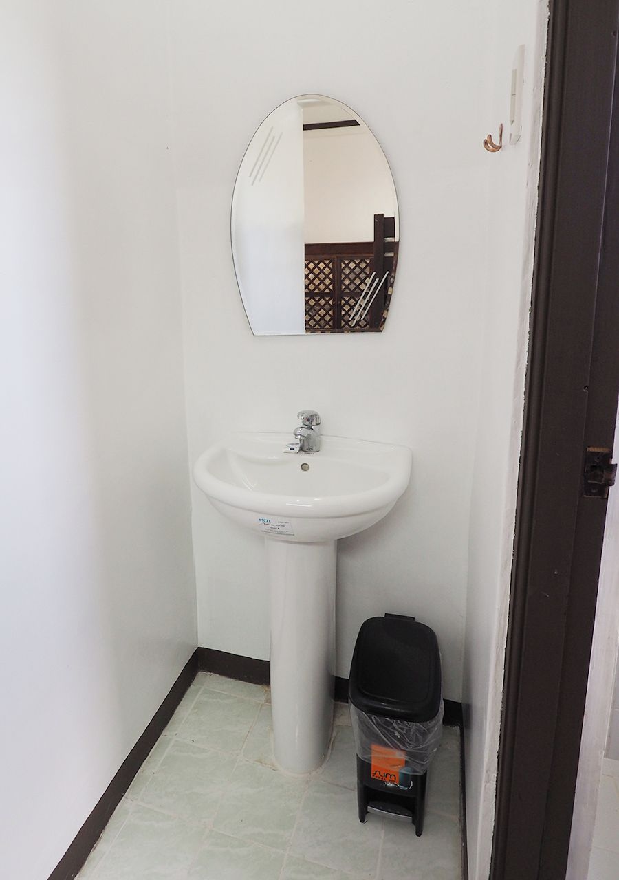 Un baño pequeño con un lavabo blanco, un espejo y un cubo de basura negro.
