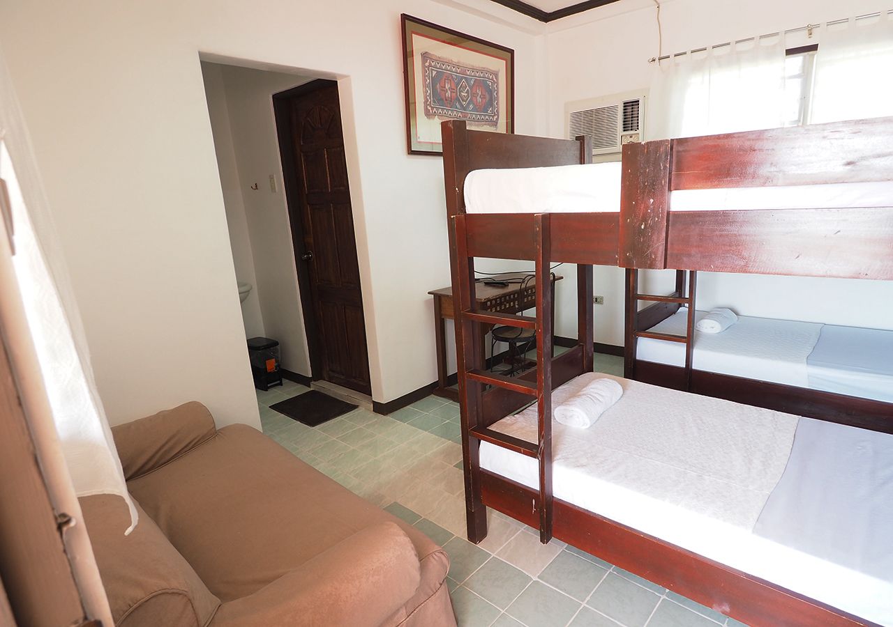 A bunk bed room with a brown sofa, a framed picture on the wall, and a door leading to another room.