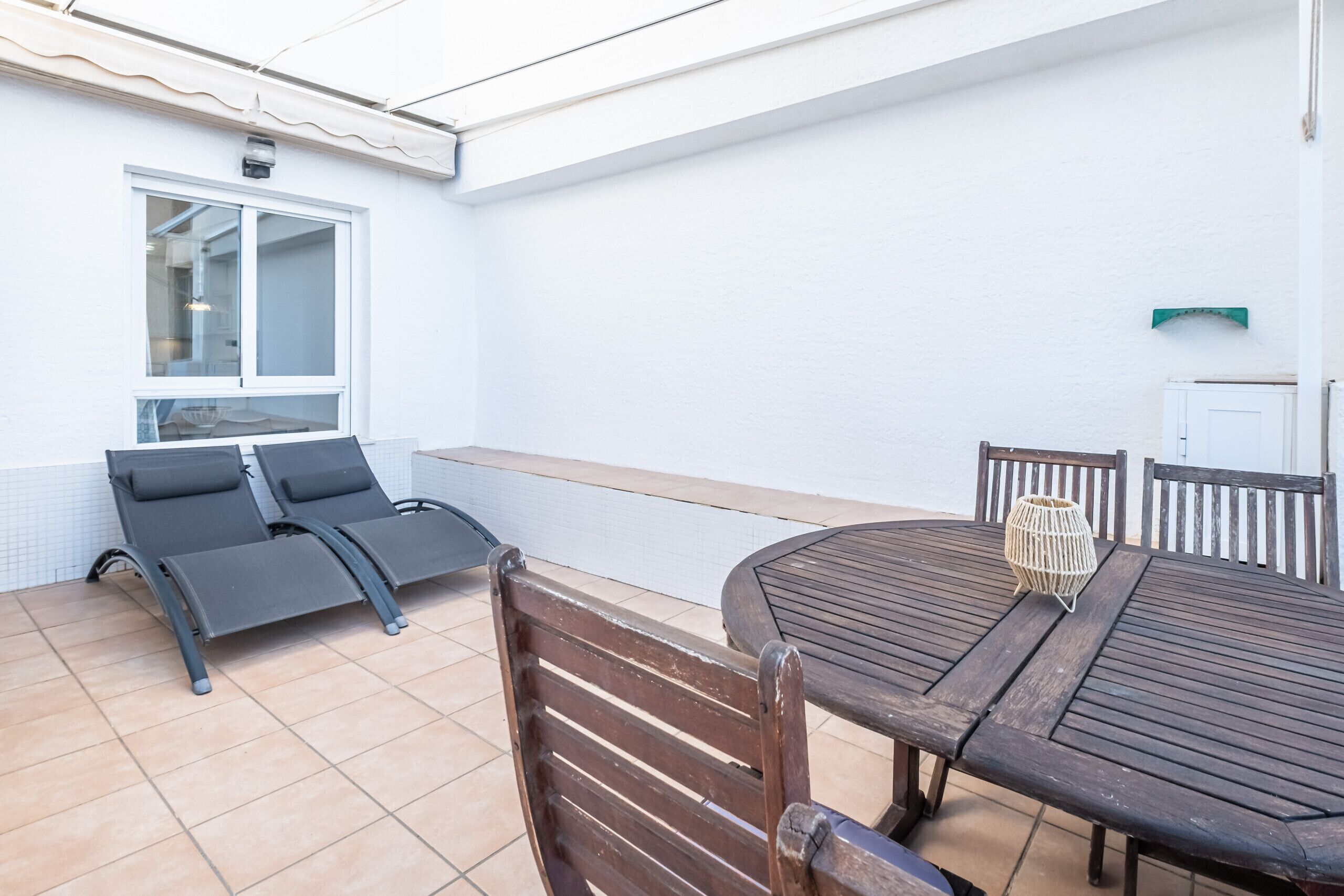 A patio with a table and chairs, a window, and a white wall.