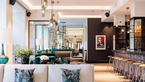 En moderne hotellobby med et siddeområde, en bar med skrammel og et stort spejl, der reflekterer indretningen.