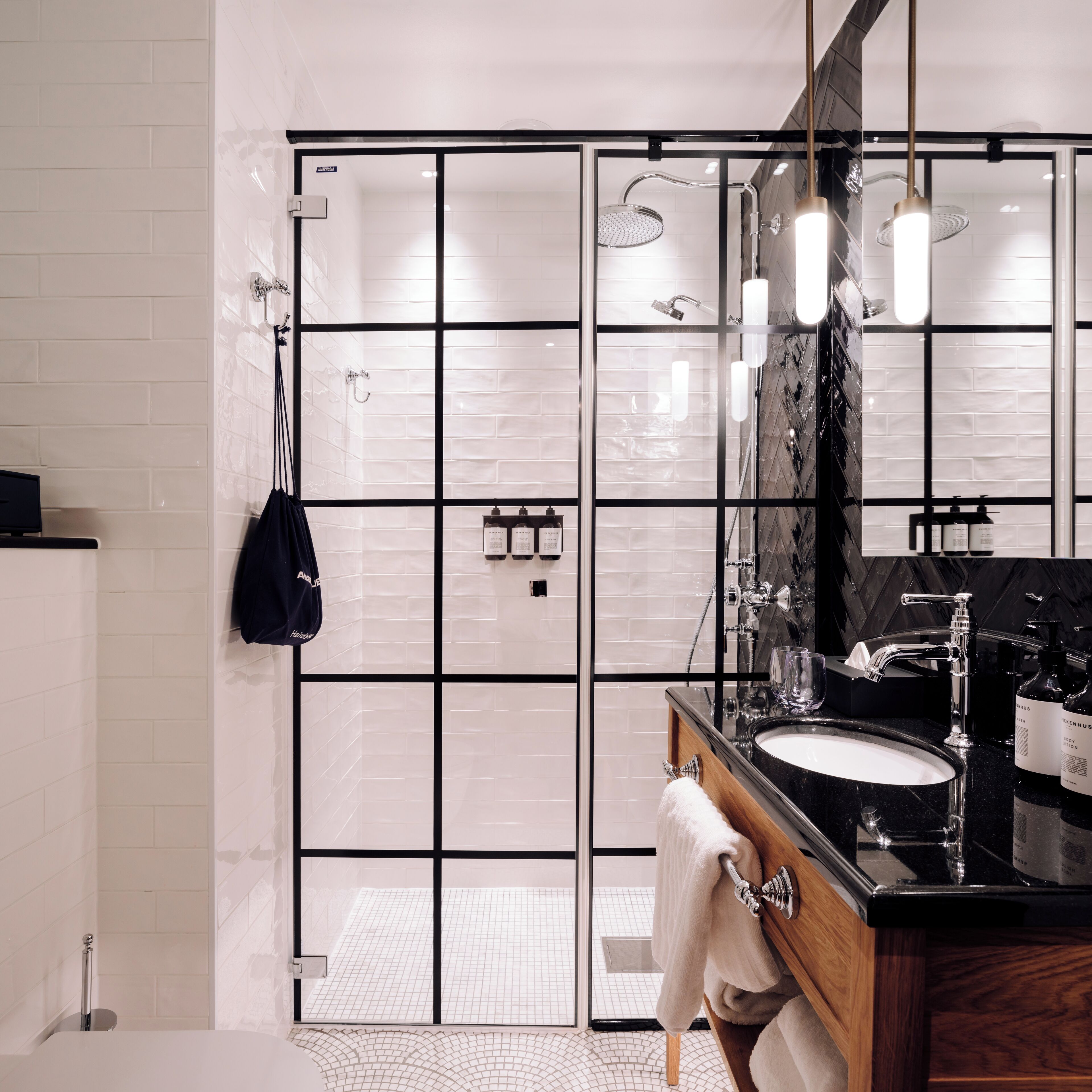 Een moderne badkamer met een douchegedeelte betegeld in zwart en wit, een houten wastafelmeubel met een zwart aanrechtblad en een grote spiegel boven de wastafel.