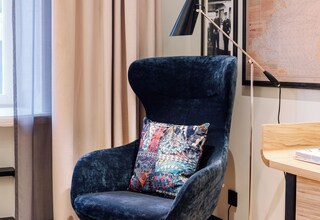 A modern room with a dark blue velvet armchair, a patterned cushion, a desk with a lamp, and a map on the wall.