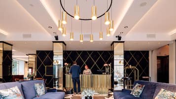 A modern hotel lobby with a reception desk, two sofas, a coffee table, and a large suitcase.