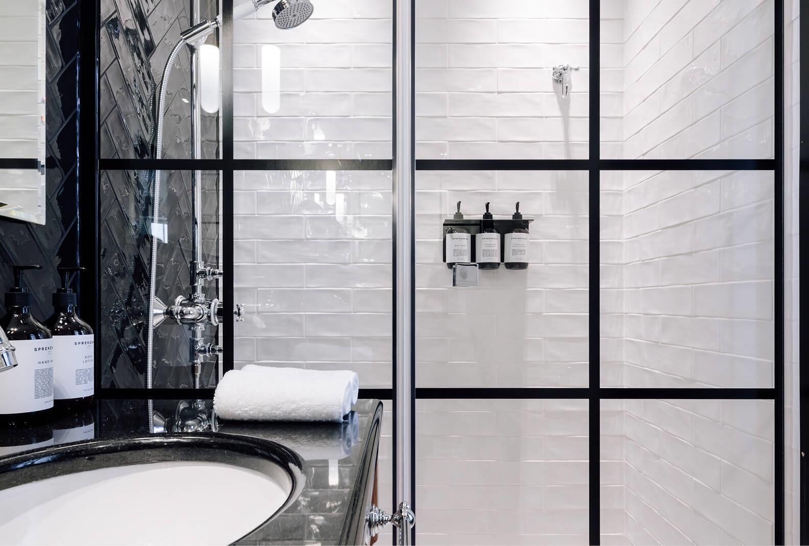 Une salle de bain moderne avec un grand miroir, une baignoire et une douche. On trouve des articles de toilette sur le comptoir et une serviette sur le sol.