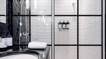 Une salle de bain moderne avec un grand miroir, une baignoire et une douche. On trouve des articles de toilette sur le comptoir et une serviette sur le sol.