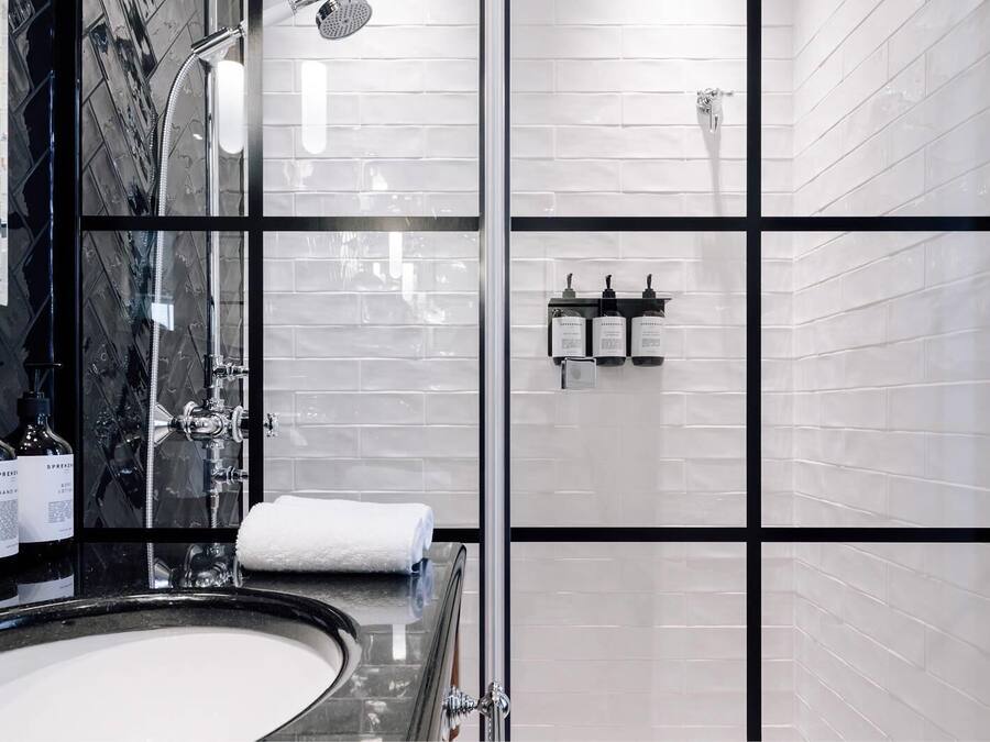 Une salle de bain moderne avec un grand miroir, une baignoire et une douche. On trouve des articles de toilette sur le comptoir et une serviette sur le sol.