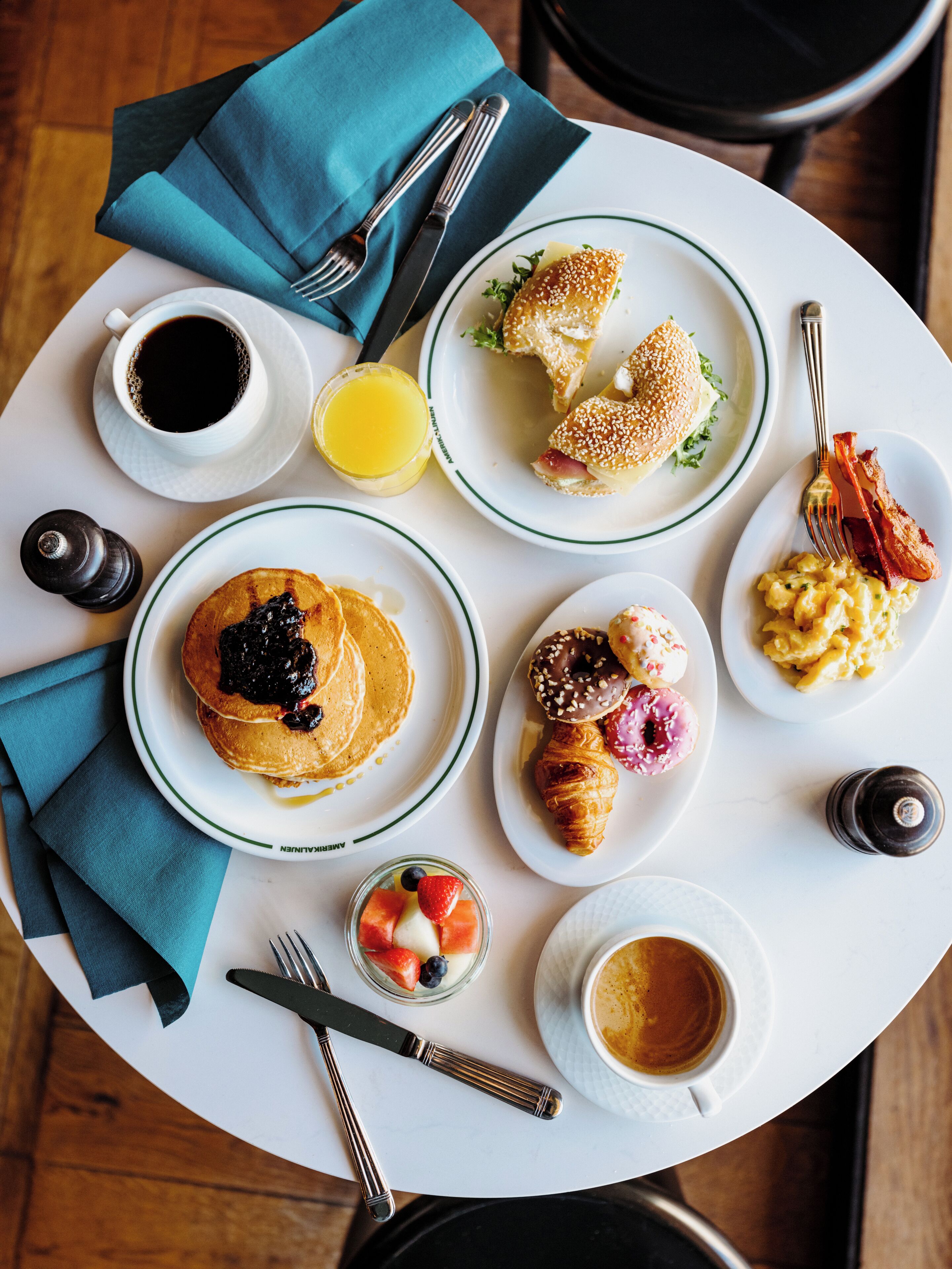 A breakfast table with plates of pancakes, croissants, and pastries, along with cups of coffee and juice.