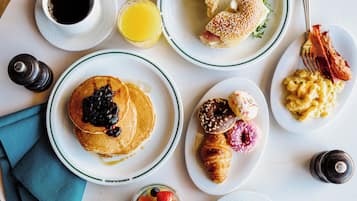 A breakfast table with plates of pancakes, croissants, and pastries, along with cups of coffee and juice.