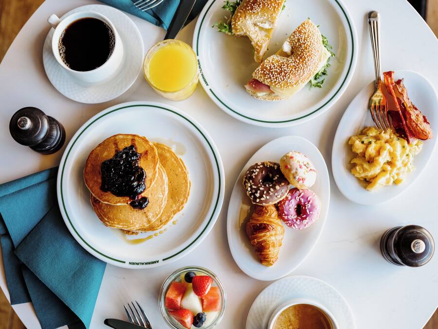 A breakfast table with plates of pancakes, croissants, and pastries, along with cups of coffee and juice.