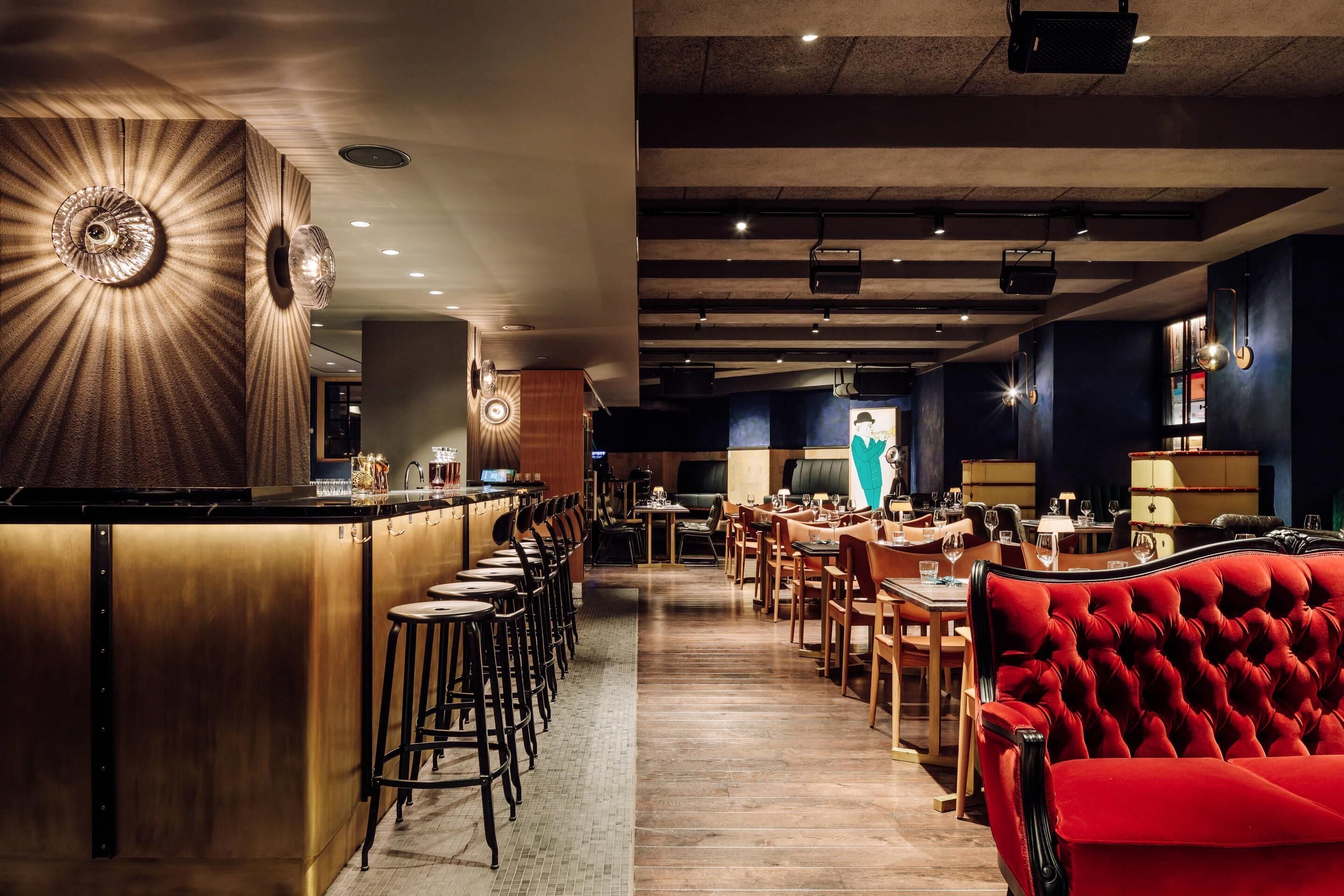 Een restaurant met een bar, hoge krukken en een rode gestoffeerde bank.