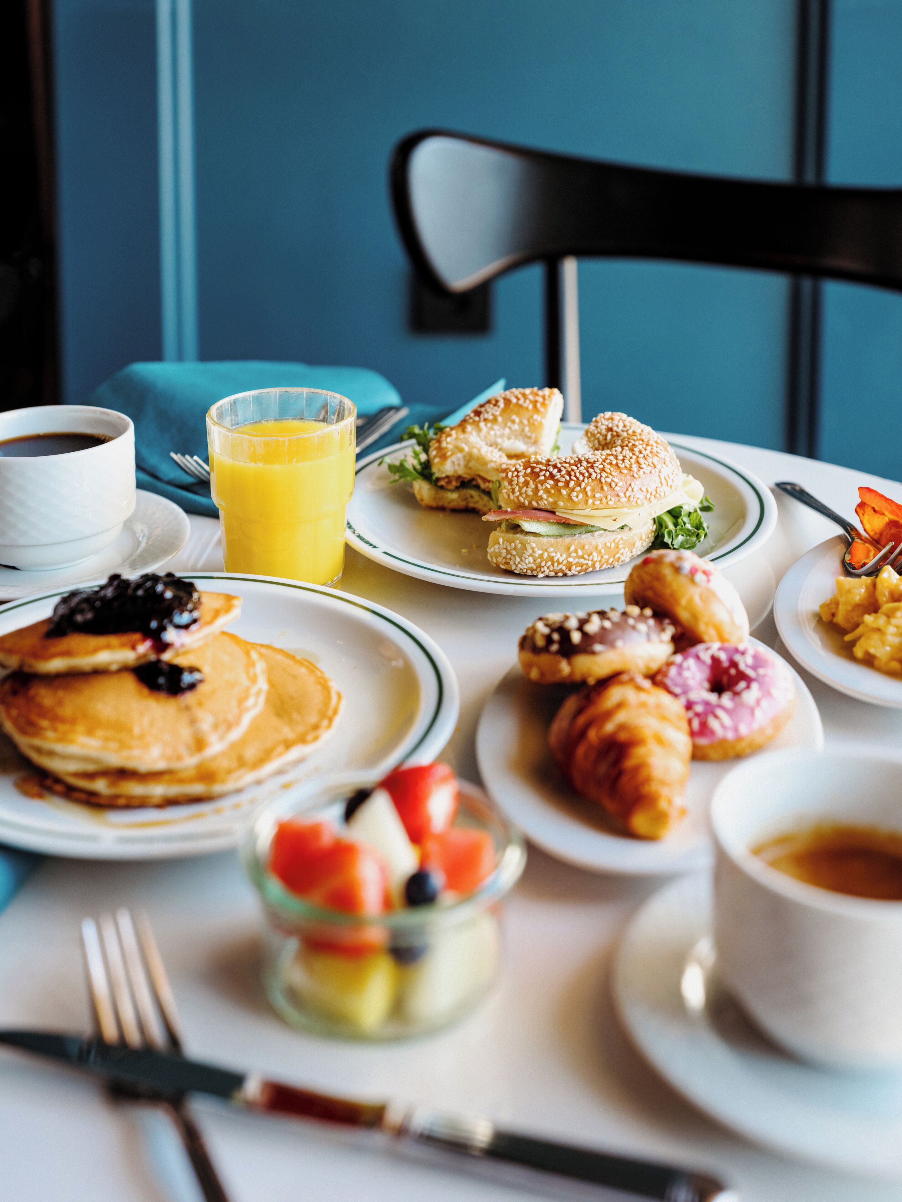 Ett frukostbord med pannkakor, en smörgås, croissanter och ett glas apelsinjuice.