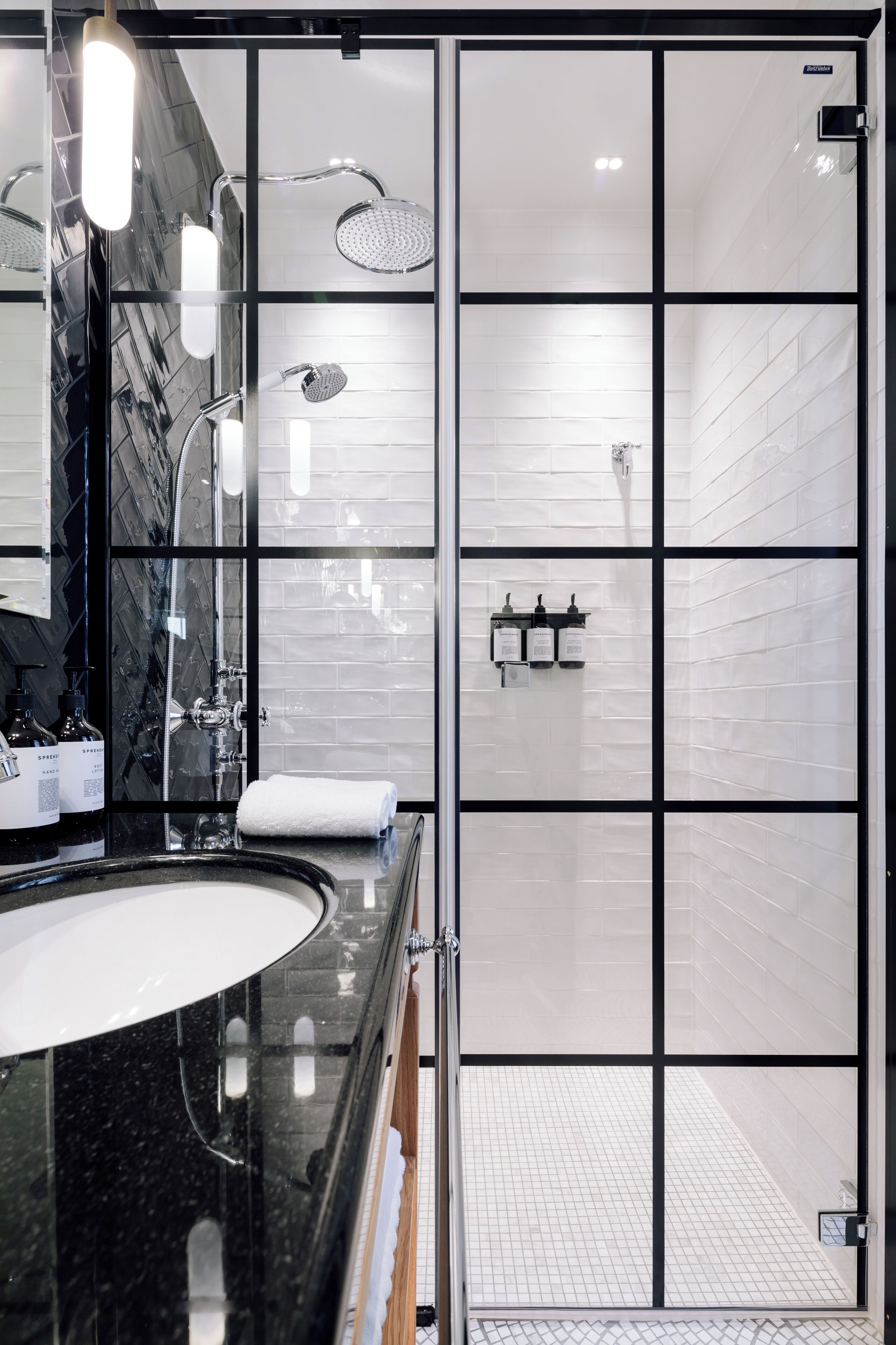 A modern bathroom with a black marble sink, a glass shower enclosure, and a white tiled shower area.